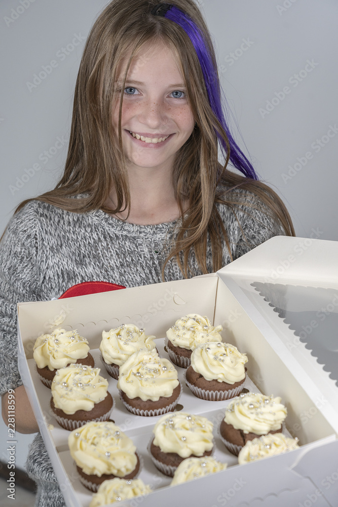 Young beautiful girl holds box of delicious cupcakes, closeup portrait indoors