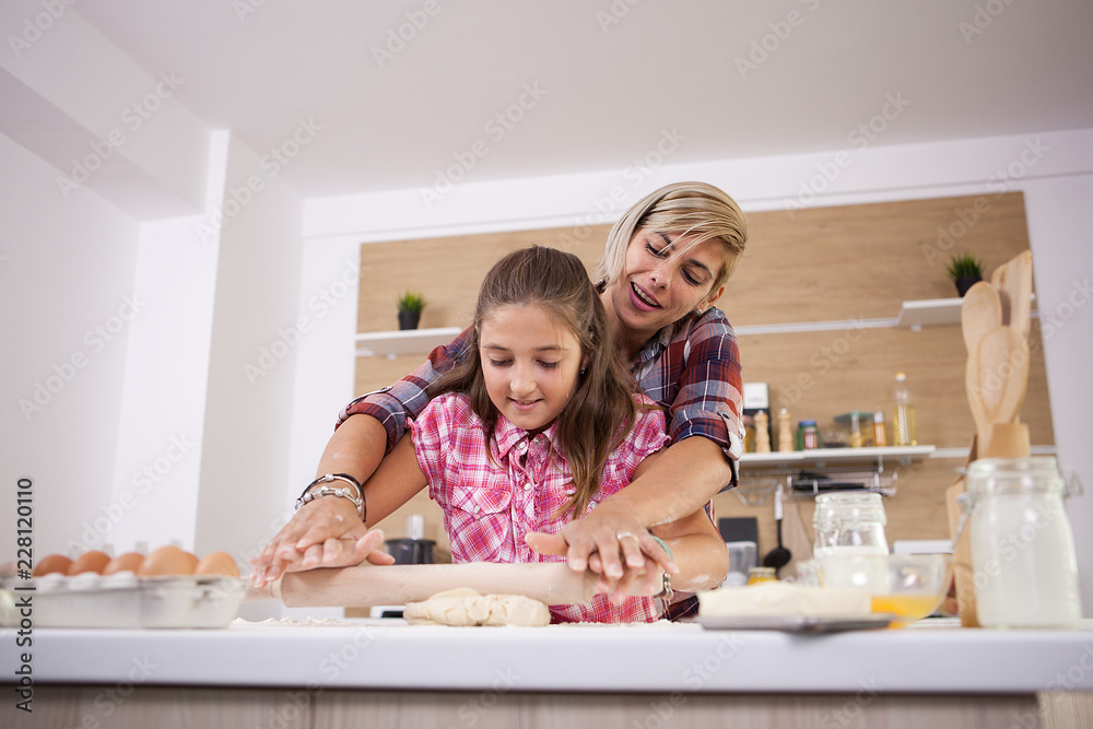 Teenage girl and her mother smiling while they are cooking together. Parent love. Teenage girl and her mother smiling while they are cooking together. Parent love.
