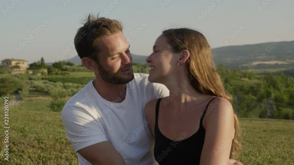 Young Couple Sitting on a Field while Kissing and Hugging Each Other Young Couple Sitting on a Field while Kissing and Hugging Each Other
