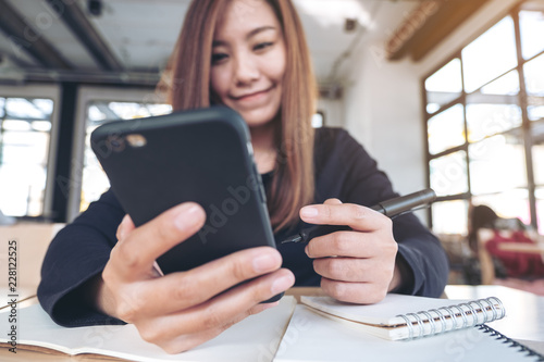 Closeup image of an Asian woman holding , using and looking at smart phone while working and writing Free Download Closeup image of an Asian woman holding , using and looking at smart phone while working and writing - GFXLoad