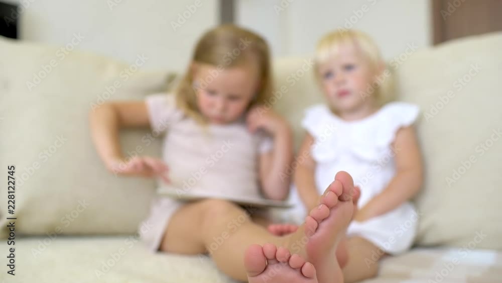 Two childs watching ang using tablet at home. Children using a modern laplop, tablet on sofa. Little girls playing on the tablet computer games, watching videos, cartoons. slow-motion Two childs watching ang using tablet at home. Children using a modern laplop, tablet on sofa. Little girls playing on the tablet computer games, watching videos, cartoons. slow-motion