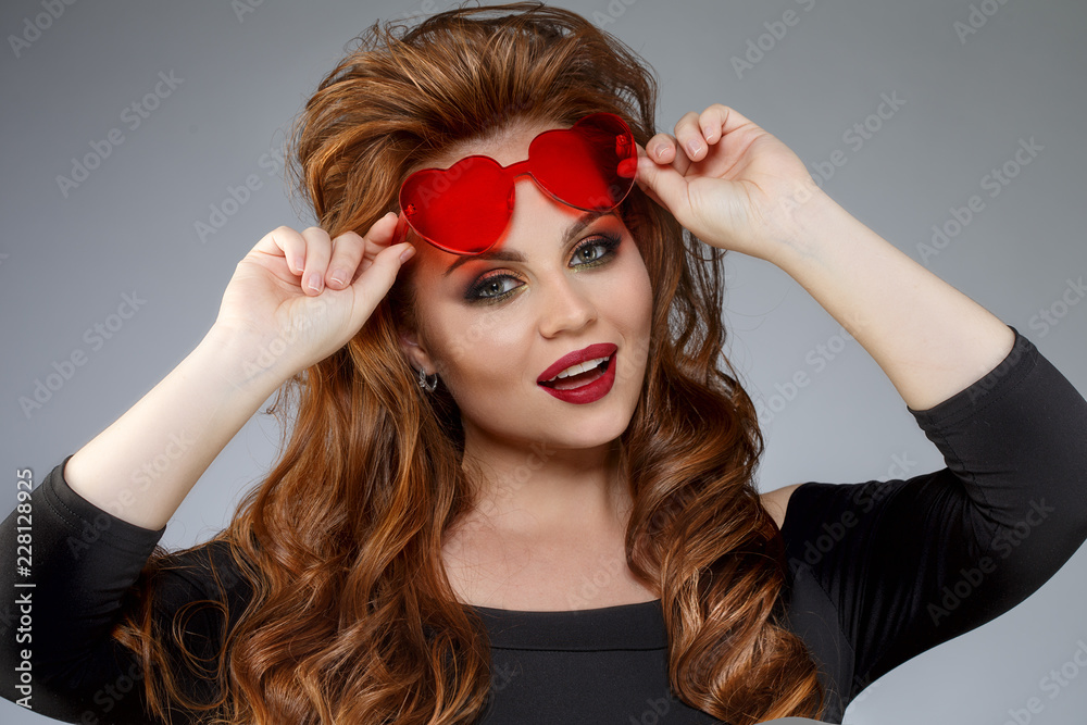 Fototapeta premium Cute girl with glasses in the shape of a heart. Funny, positive, funny model in red sunglasses.