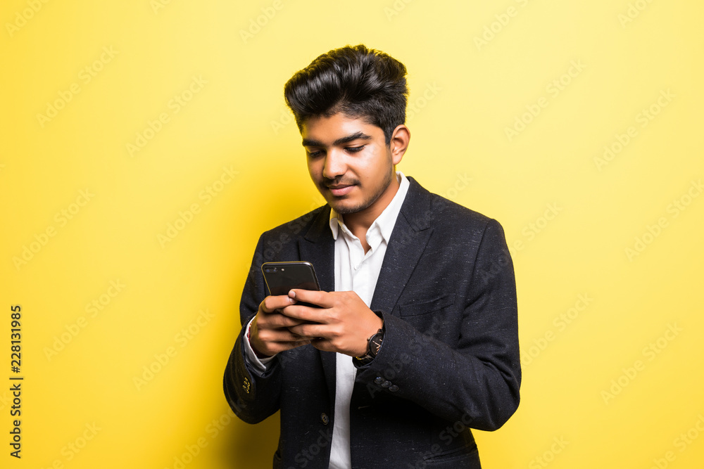 Handsome young man using mobile phone isolated on yellow background Handsome young man using mobile phone isolated on yellow background