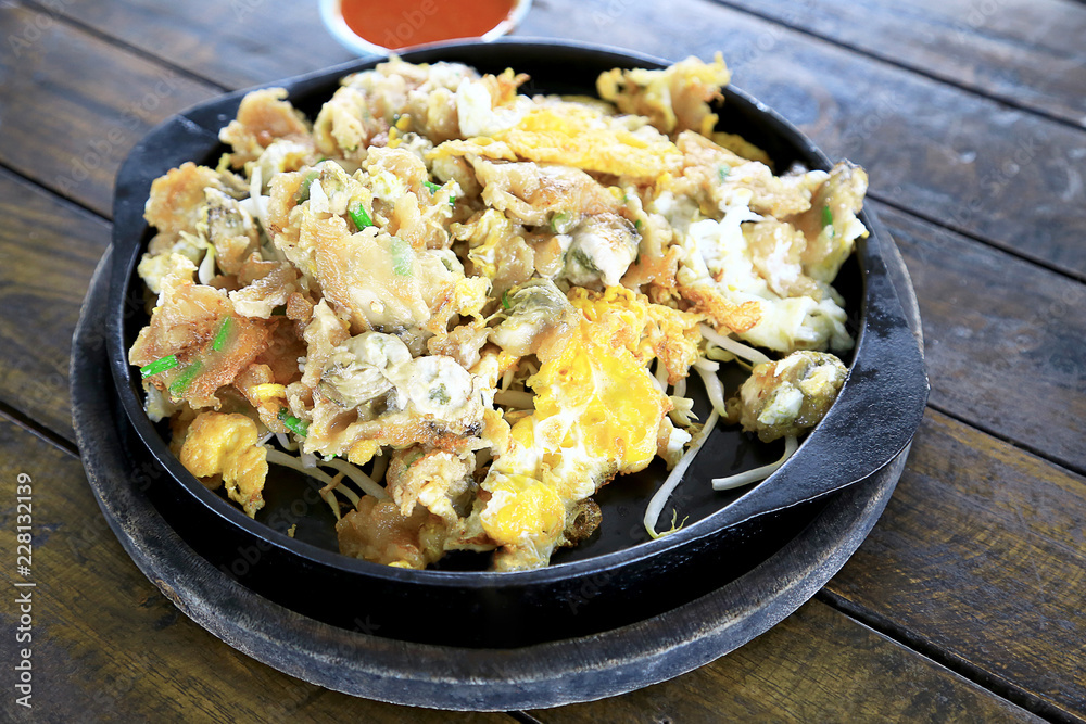 Oyster omelette in the hot pan with chili sauce on wooden table background. Foods concept. Oyster omelette in the hot pan with chili sauce on wooden table background. Foods concept.