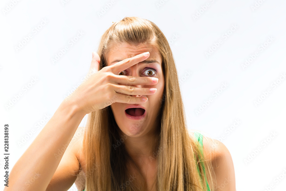 Close-up of afraid woman looking through fingers over the face against white background Close-up of afraid woman looking through fingers over the face against white background