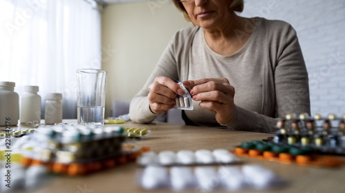 Unhealthy elderly lady drinking pills, vitamins, illness symptoms, hypochondria photo