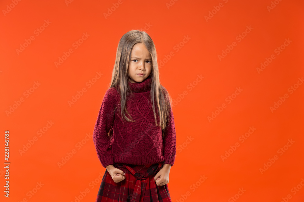 Angry teen girl standing on trendy studio background. Female half-length portrait. Human emotions, facial expression concept. Front view.