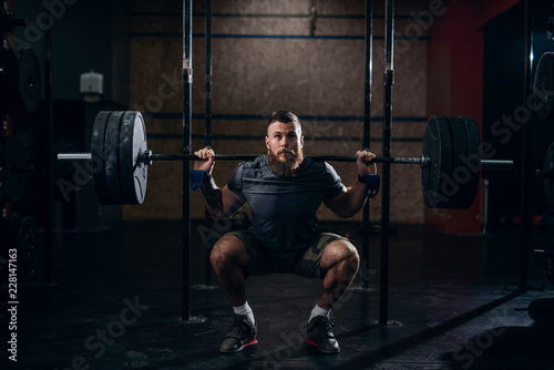 Muscular caucasian bearded man lifting weights and doing back squat in gym. photo