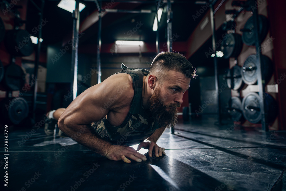 Muscular caucasian bearded man doing push-ups in military style weighted  vest in gym. Weight plates in background. foto de Stock | Adobe Stock