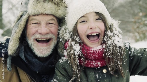 A close-up of grandfather and small girl in snow on a winter day.