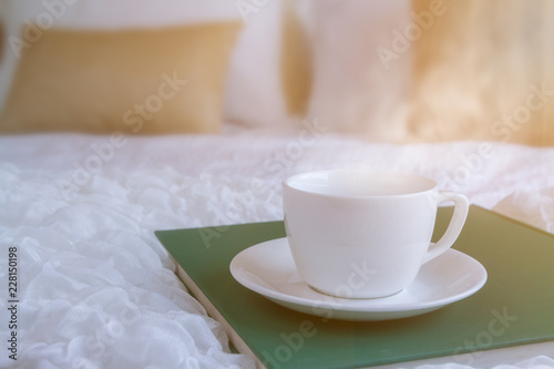 White coffee cup put on green plate in the bed room with soft streme smoke and window lighting. Background process by sunlight effect as a morning. Selective focus and copy space