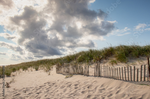 sand dunes with beach fence with blue sky and clouds
