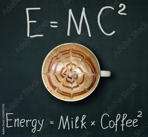 The cup of coffee with milk and two formulas. E = mc2. Black background.