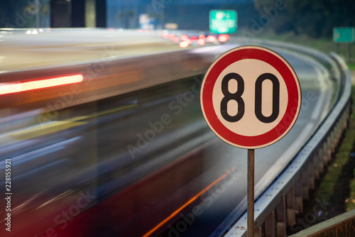 Long exposure shot of traffic sign showing 80 km/h speed limit on a highway full of cars in motion blur during the night