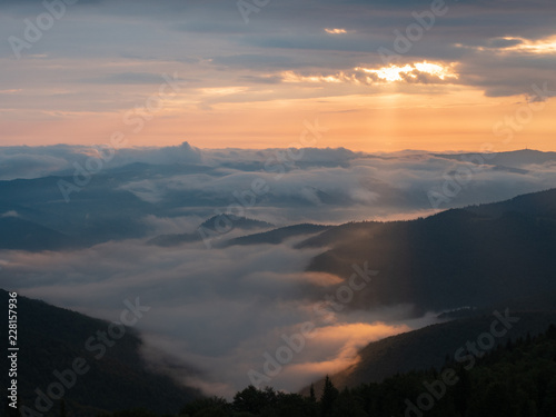 Background of Ukrainian mountains at summer. Sunset in west Ukraine. Carpathians mountains in august. Sun beams illuminating the clouds flowing between high peaks. Blurred background