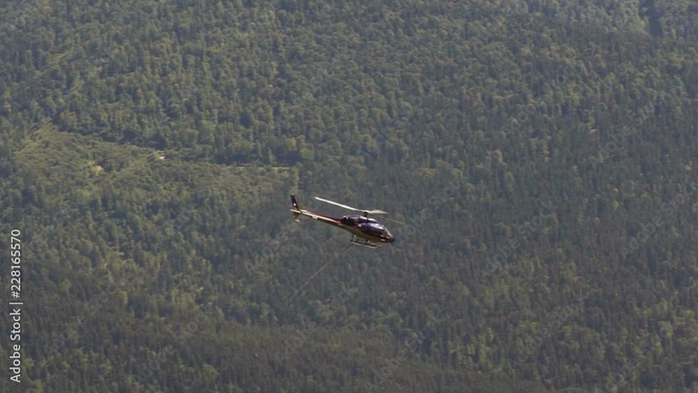 Slow-motion of a close up helicopter flying over a mountain and a city carrying construction materials Slow-motion of a close up helicopter flying over a mountain and a city carrying construction materials
