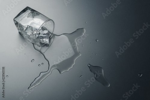 close up of a glass of water with ice cubes spilled on the table
