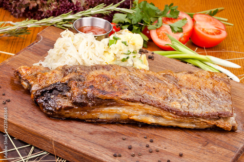 Pork ribs with potato salad on wooden cutting board. Close up