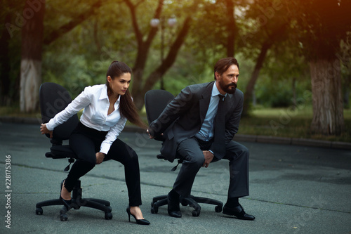 Man and woman sitting on office chairs outside. Looking aside. Ready to start.