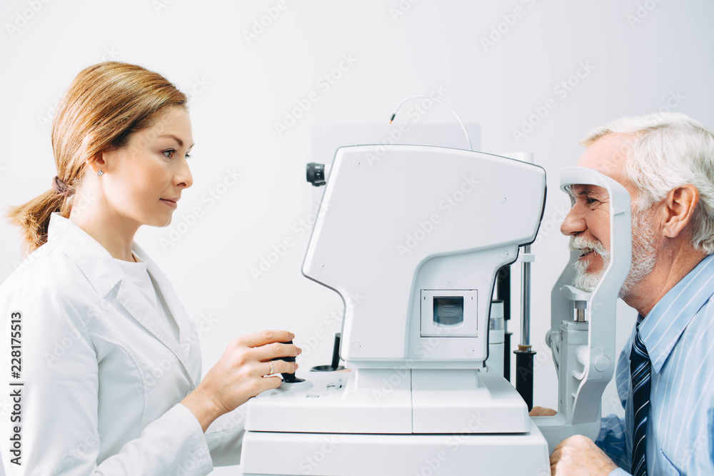 Doctor Optometrist examining old man's eyes with special eye equipment - obrazy, fototapety, plakaty 