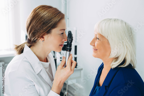 Doctor Optometrist examining senior woman's eye with ophthalmoscope photo