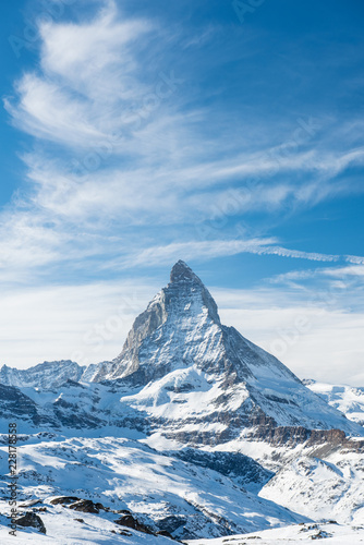 Scenic view on snowy Matterhorn peak in sunny day with blue sky and dramatic clouds in background, Switzerland