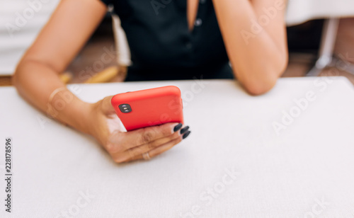 Cropped image of business woman reading news on smart phone indoor in a cafe. Smiling young female texting messages on mobile phone in the restaurant. Elegant lady shopping via free wireless on phone