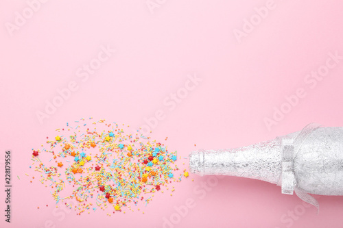 Champagne bottle with colorful sprinkles on pink background