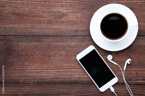 Smartphone with earphones and cup of coffee on wooden table