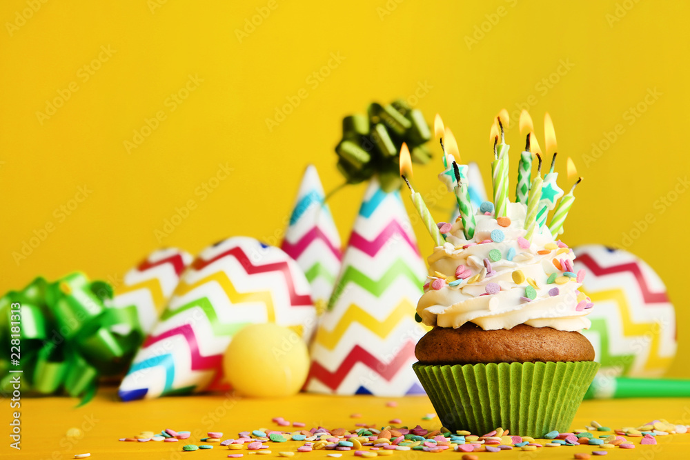 Cupcake with candles and paper caps on yellow background