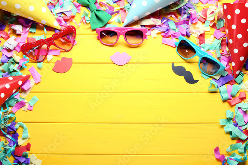 Sunglasses with paper caps and confetti on yellow wooden table