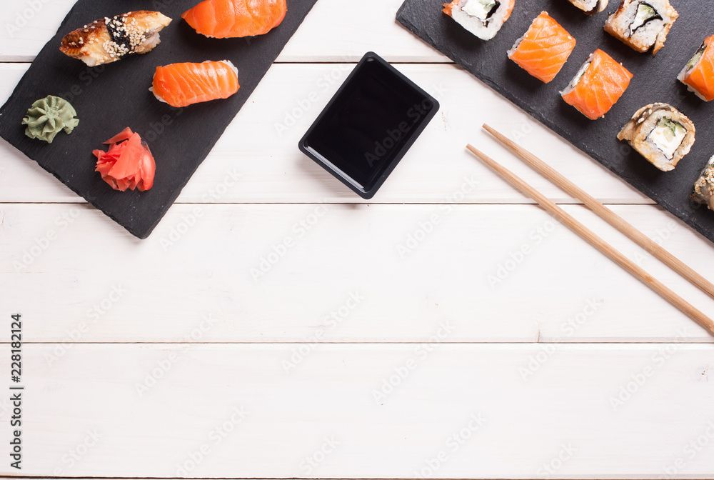 Japanese sushi rolls and sushi set with salmon and cream cheese on stone slate with chopsticks and soy sauce and ginger on wooden background copy space. Japanese sushi rolls and sushi set with salmon and cream cheese on stone slate with chopsticks and soy sauce and ginger on wooden background copy space.