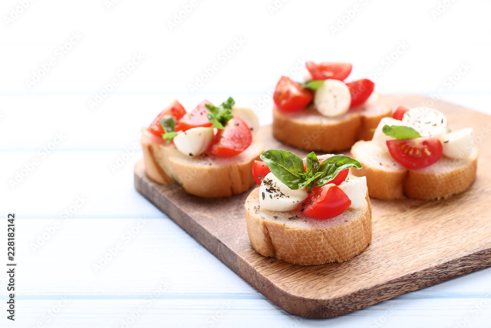 Bruschetta with mozzarella, tomatoes and basil leafs on wooden cutting board