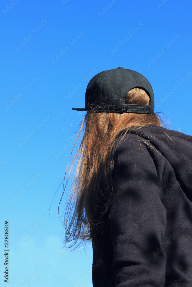 Stockfoto Young Girl Wearing Casual Women Fashion Clothes: Hoodie and  Snapback Cap, Back Side Portrait. Stylish Female in All Black Clothes  Standing Alone, Facing Away on Empty Blue Sky Background | Adobe
