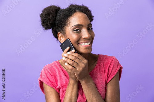 Photo of positive african american woman smiling and talking on mobile phone, isolated over violet background