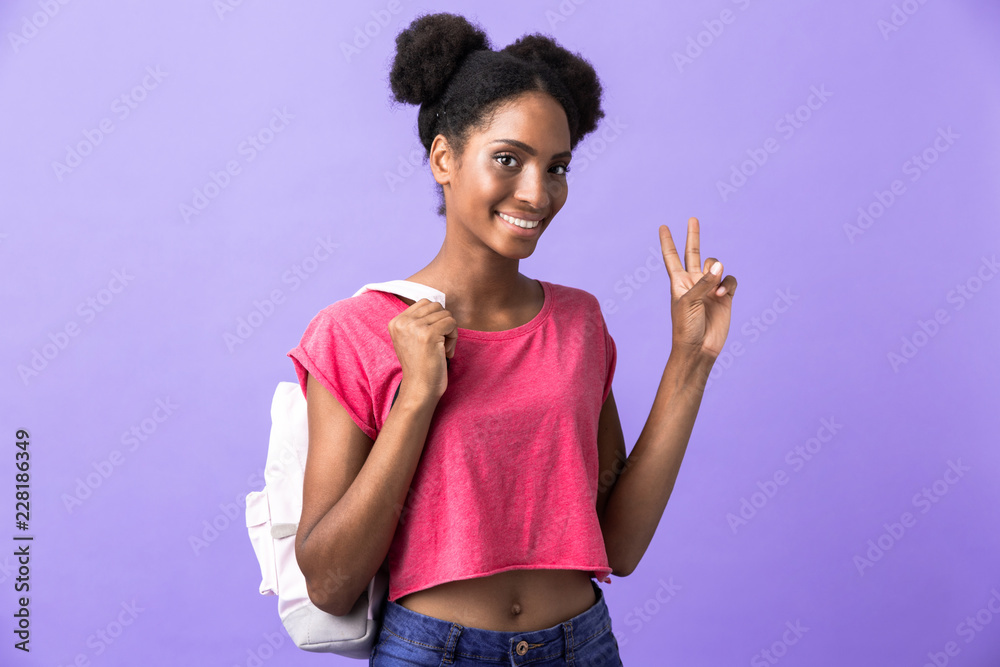 Photo of brunette african american woman student wearing backpack showing peace sign, isolated over violet background