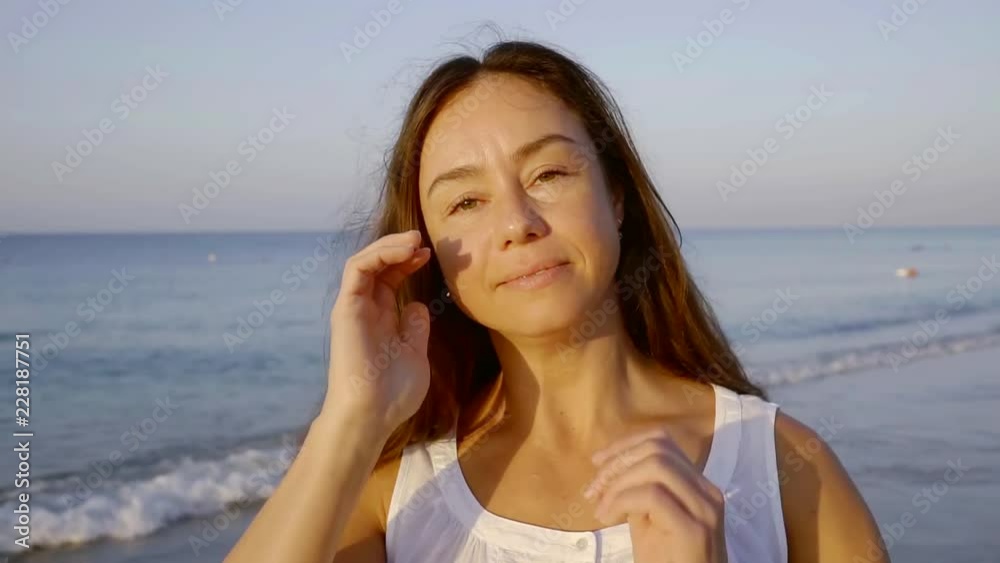 charming adult brunette woman is smiling and looking at camera, standing on ocean coast in summer charming adult brunette woman is smiling and looking at camera, standing on ocean coast in summer