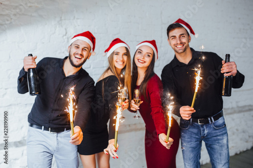 Four young friends hold champagne and fireworks in their hands  they are happy and celebrate the new year.