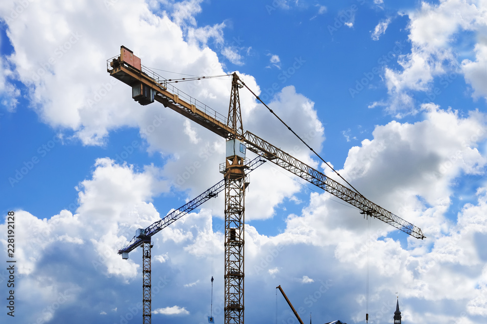 Construction tower cranes against a partly cloudy bright blue sky
