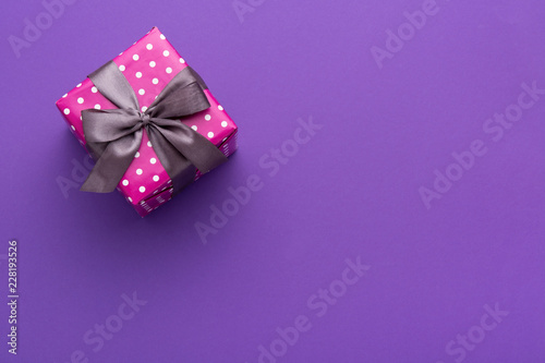 Wrapped gift box with colored ribbon as a present for Christmas, new year, mother's day, anniversary, birthday, party,  on violet background, top view. Present for a colleague at work.