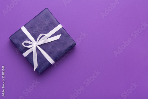 Wrapped gift box with colored ribbon as a present for Christmas, new year, mother's day, anniversary, birthday, party,  on violet background, top view. Present for a colleague at work.