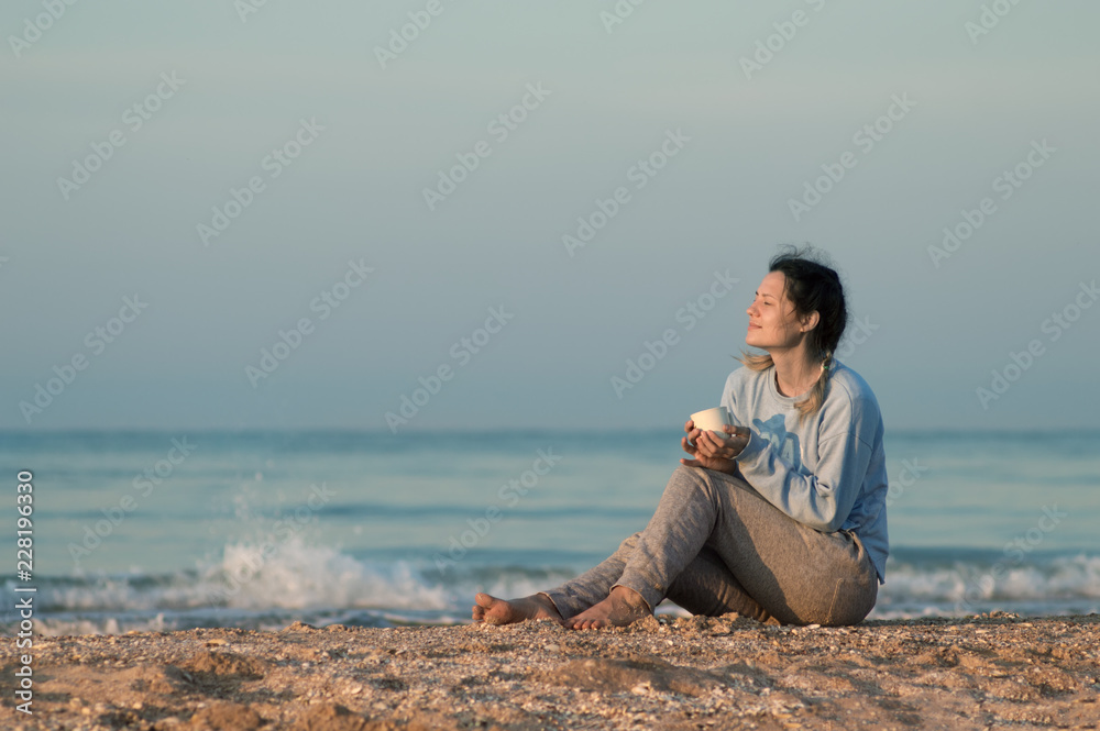 girl sitting on the sandy shore, the sea, cold, drink in the hands