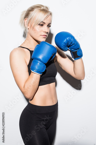 Beautiful smiling young fitness woman wears blue boxing gloves over grey background