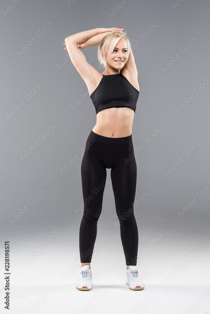Portrait of a smiling fitness woman stretching her hands isolated over gray background Portrait of a smiling fitness woman stretching her hands isolated over gray background