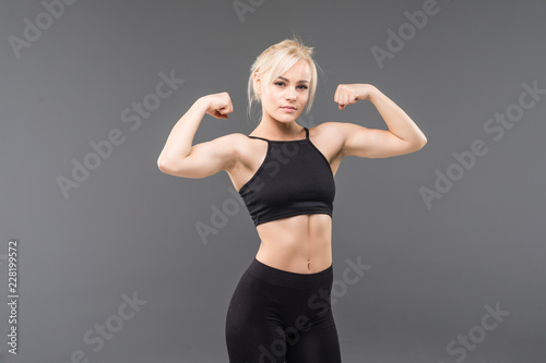 Young sporty woman looking at her biceps isolated on gray background