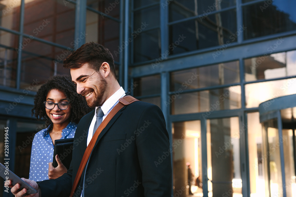 Businesspeople walking out of office building with digital table Businesspeople walking out of office building with digital table