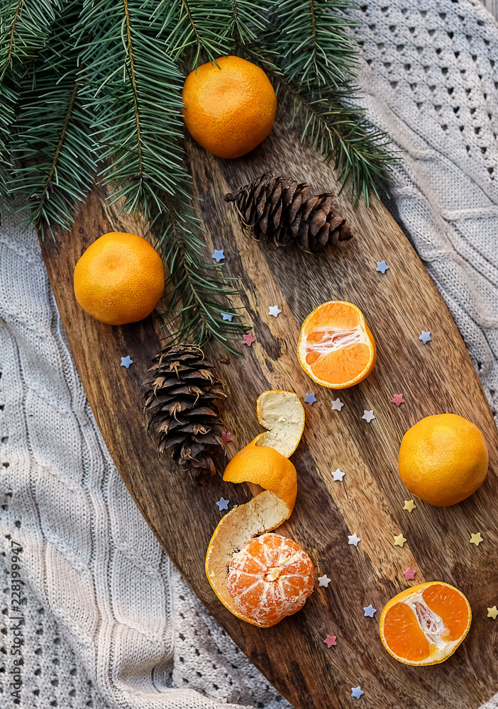 Sweet tangerines, fir tree brunches, pine cones on wooden kitchen board in rustic style on wooden background and gray knitted plaid. Christmas food decorations. Table setting. Flat lay copy space. Sweet tangerines, fir tree brunches, pine cones on wooden kitchen board in rustic style on wooden background and gray knitted plaid. Christmas food decorations. Table setting. Flat lay copy space.