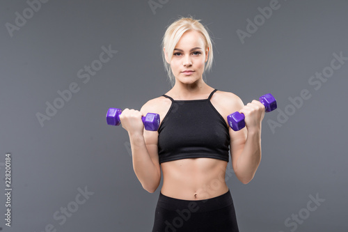 Portrait of a pretty young sportswoman doing exercises with dumbbells isolated on a gray background