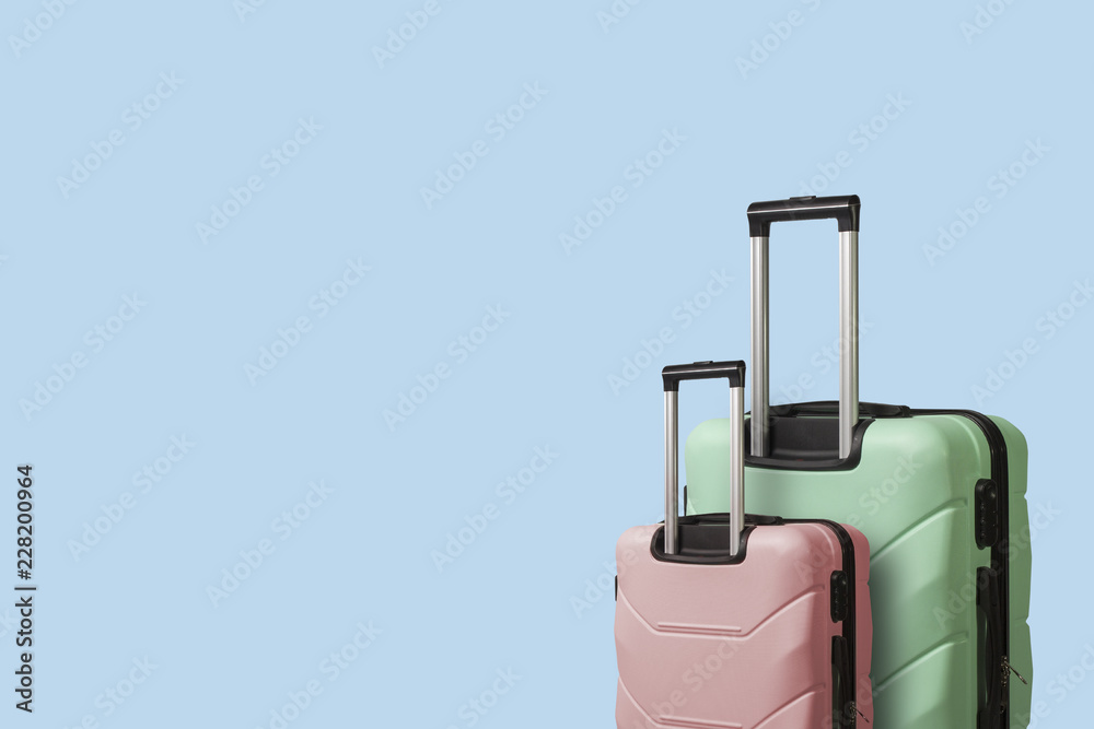 Two Suitcases on wheels on a blue background. Сoncept of travel, a vacation trip, a visit to relatives. Pink and Green color Two Suitcases on wheels on a blue background. Сoncept of travel, a vacation trip, a visit to relatives. Pink and Green color