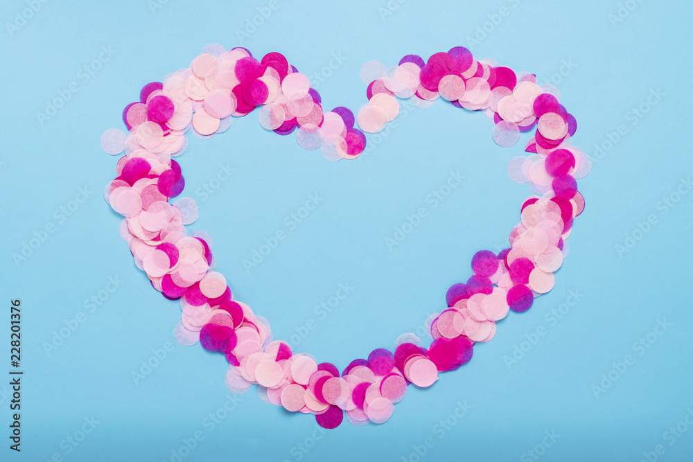 Heart shaped pink confetti on a blue background. Party and holiday concept. Flat lay, top view